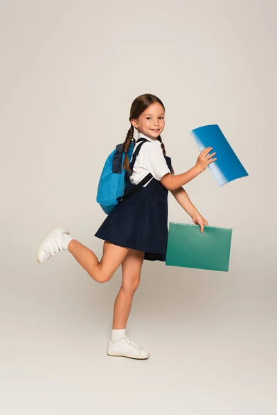 Volledige Weergave Van Vrolijke Schoolkind Lopen Met Notebooks Grijs — Stockfoto
