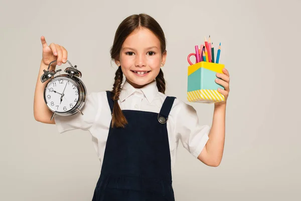 Pleased Schoolkid Showing Pen Holder Large Alarm Clock Isolated Grey — Stock Photo, Image