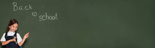 happy schoolgirl pointing at chalkboard with back to school lettering, banner