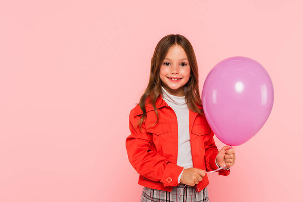 stylish girl with festive balloon smiling at camera isolated on pink