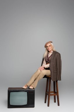 Gri arka planda retro televizyonun yanındaki sandalyede oturan zarif kadın. 