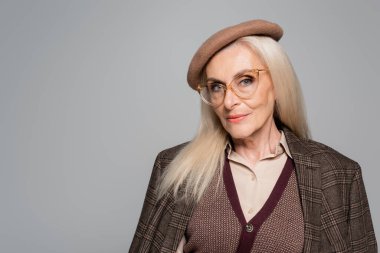 Ekose ceketli ve bereli şık bir son sınıf öğrencisi gri kameraya bakıyor. 