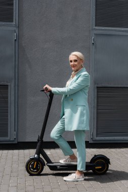 Elektrikli scooter 'ın yanında duran gülümseyen yaşlı iş kadını. 