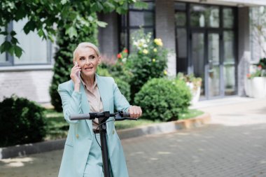Elektrikli scooter 'ın yanında cep telefonuyla konuşan kıdemli iş kadını. 