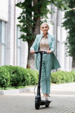 Mavi takım elbiseli yaşlı bir iş kadını dışarıda elektrikli scooter kullanıyor.