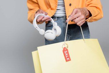 Kulaklık ve satış etiketli alışveriş çantası taşıyan yaşlı bir kadının gri renkli görüntüsü.