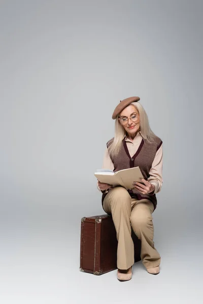 Elderly Woman Beret Reading Book Retro Suitcase Grey Background — Stock Photo, Image