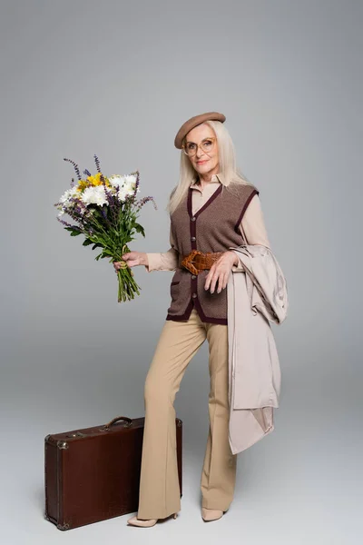 Smiling Senior Woman Trench Coat Flowers Looking Camera Vintage Suitcase — Stock Photo, Image