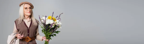 Äldre Kvinna Basker Med Blommor Och Trenchcoat Isolerad Grå Banner — Stockfoto