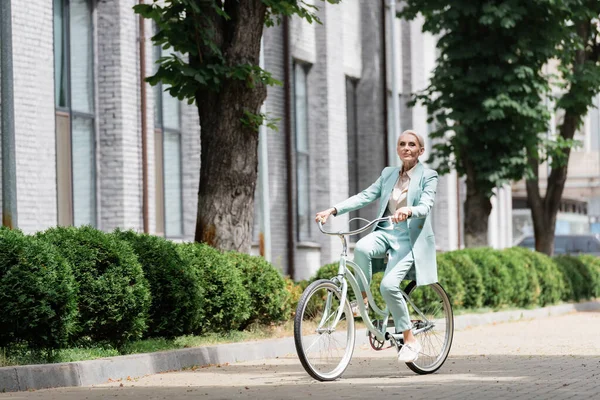 青いスーツを着た高齢の実業家が自転車に乗って — ストック写真