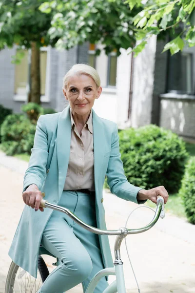 Grauhaarige Geschäftsfrau Auf Fahrrad Lächelt Draußen Die Kamera — Stockfoto