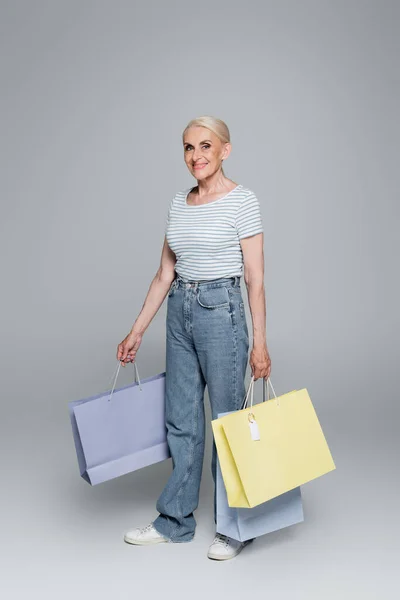 Happy Senior Woman Jeans Holding Shopping Bags Grey — Stock Photo, Image