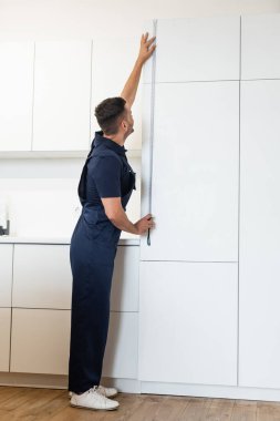 Üniformalı ustabaşının mutfaktaki mobilyaları ölçerken tam boy görünümü