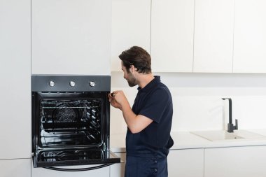 Modern mutfakta elektrikli fırını tamir eden bir işçi.