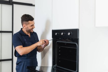 Gülümseyen işçi tornavidayla elektrikli fırını tamir ediyor.