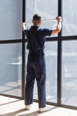 back view of workman in overalls measuring large windows clipart