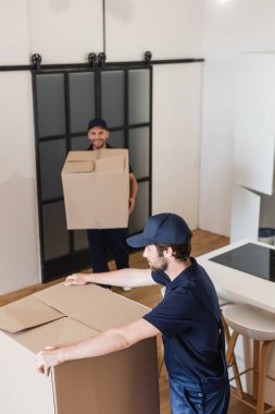 blurred mover holding carton box near colleague in kitchen clipart