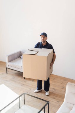 mover holding big cardboard box in apartment  clipart