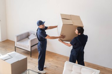 Üniformalı tamirciler oturma odasında karton kutu taşıyorlar.