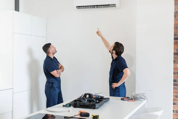 Reparaturarbeiter Zeigt Auf Klimaanlage Der Nähe Des Kollegen Und Werkzeug — Stockfoto