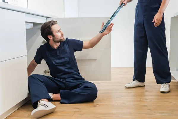 Worker Giving Adjustable Wrench Plumber Sitting Floor Kitchen — Stock Photo, Image