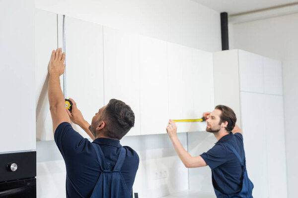 механики, измеряющие белую мебель на современной кухне