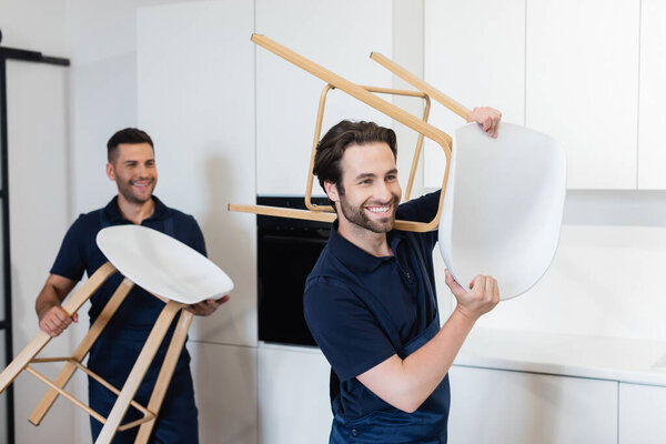 smiling movers carrying white stools in kitchen