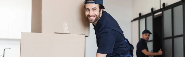 Glücklicher Mover Lächelnd Neben Pappverpackungen Und Verschwommenem Kollegen Banner — Stockfoto