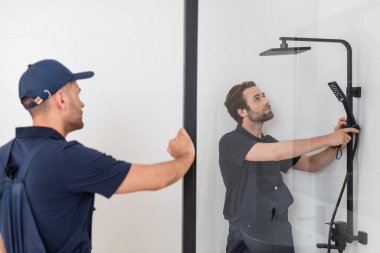 blurred foreman looking at colleague checking shower in bathroom clipart