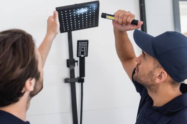 plumber checking shower head in bathroom with flashlight clipart