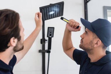 plumbers with flashlight looking at shower head in bathroom clipart