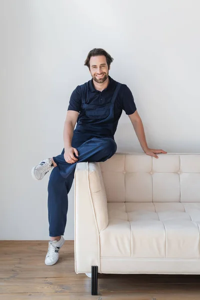 Mandor Berseragam Dan Sepatu Tersenyum Pada Kamera Sofa Putih — Stok Foto
