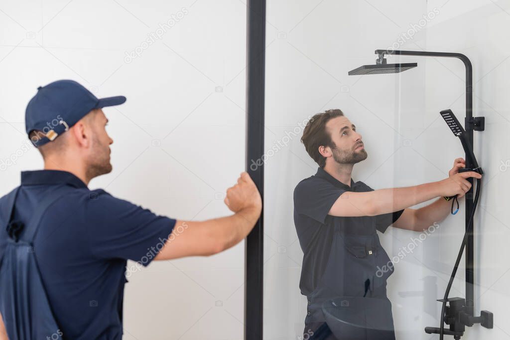 blurred foreman looking at colleague checking shower in bathroom