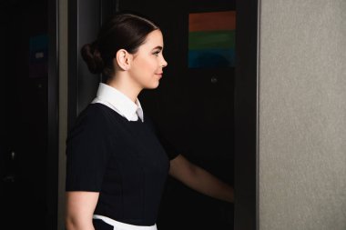 young maid knocking door in corridor of hotel room clipart