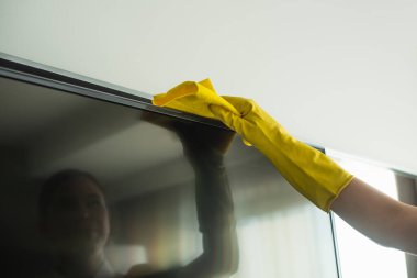 Lastik eldivenli temizlikçi, televizyon ekranını paçavrayla temizliyor.