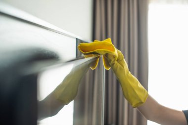 partial view of housekeeper in rubber glove cleaning tv display with rag clipart