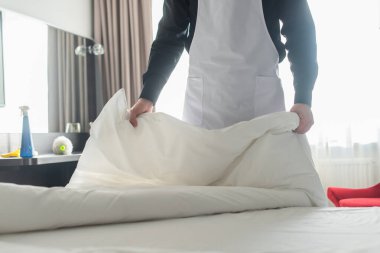 Otel odasında beyaz yatak değiştiren hizmetçi manzarası.