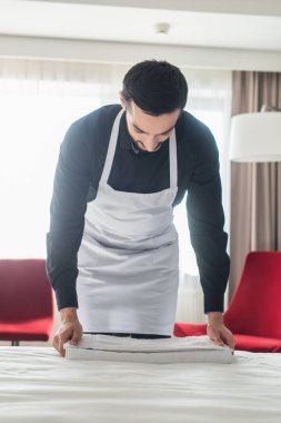 Sakallı hizmetçi otel odasındaki yatağa temiz havlu koyuyor. 