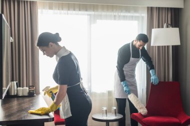 Temizlikçiler modern otel odasını temizlik malzemeleriyle temizliyor.