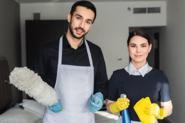 Mutlu temizlikçiler temizlik malzemelerini tutarken kameraya bakarlar.