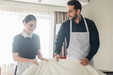 smiling housekeepers changing bedding in hotel room  clipart