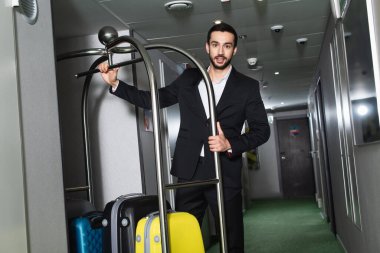 Otelin koridorunda bagajı olan metal çan arabasının yanında sakallı belboy.