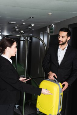 Bulanık resepsiyonist akıllı telefon tutuyor ve valizli kominin yanına işaret ediyor. 