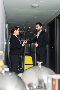 Akıllı telefon tutan ve valiz arabalı belboy ile konuşan resepsiyonist.