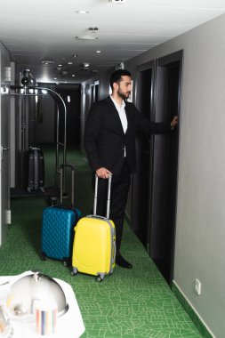 Bavulun yanında duran ve otelin kapısını çalan takım elbiseli komi.