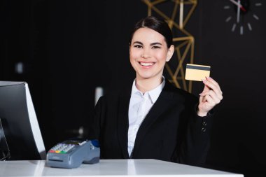 Otel ödeme terminalinin yanında kredi kartı tutan mutlu bir yönetici.