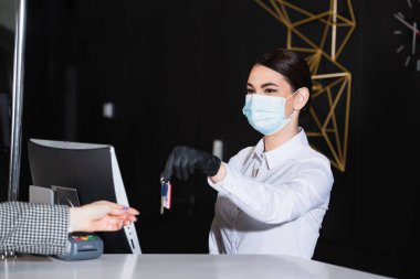 Tıbbi maskeli resepsiyonistin elinde misafir odasının bulanık anahtarı var. 