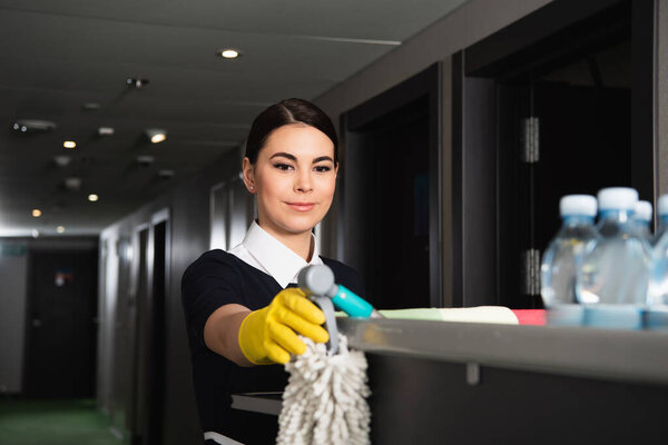 young maid in rubber glove reaching mop on housekeeping cart 