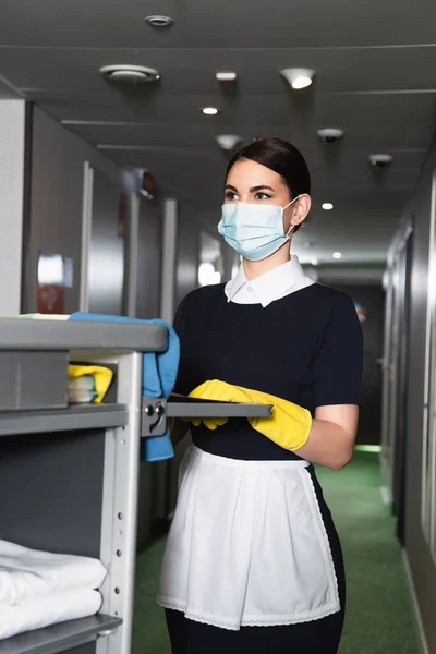 Tıbbi Maskeli Genç Oda Hizmetçisi Temizlik Arabasının Sapını Tutuyor — Stok fotoğraf