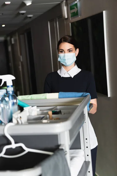 Ung Kammarjungfru Medicinsk Mask Står Nära Suddig Städvagn — Stockfoto